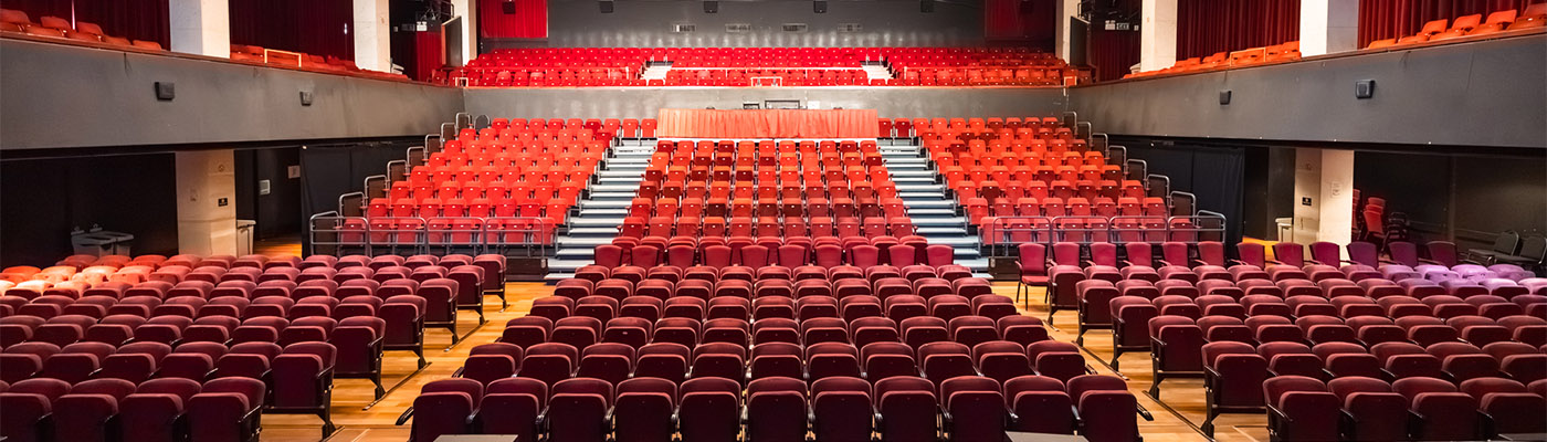 A large, empty Alban Arena auditorium with rows of red seats facing a stage with red curtains.