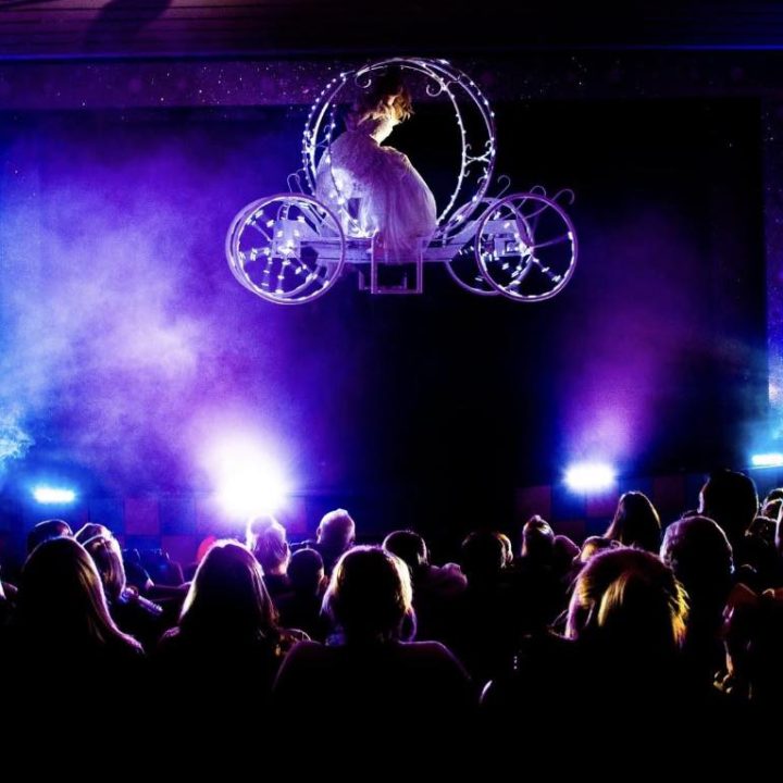 A performer in a white costume is suspended inside a floating carriage.
