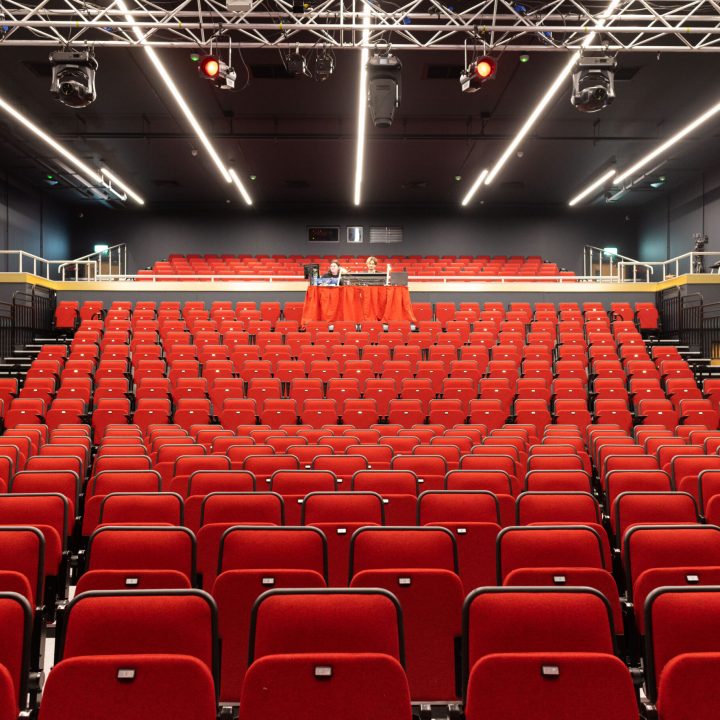 Empty theater auditorium with rows of red seats and a view of the stage.