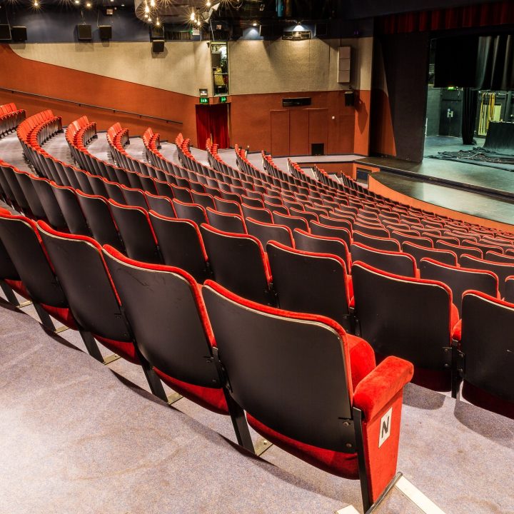 Empty Gordon Craig theatre with curved rows of black and red seats facing a stage.
