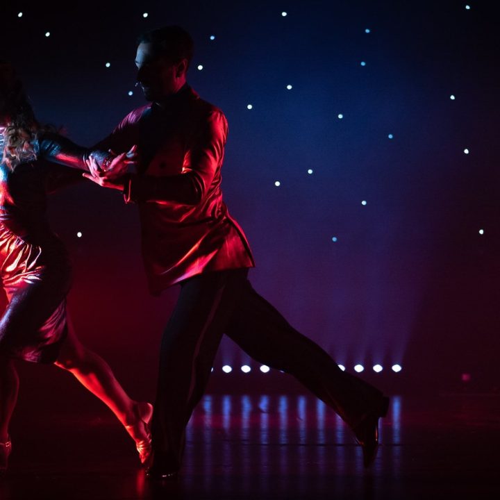 Two dancers performing on stage. The male dancer is dressed in a red shirt.