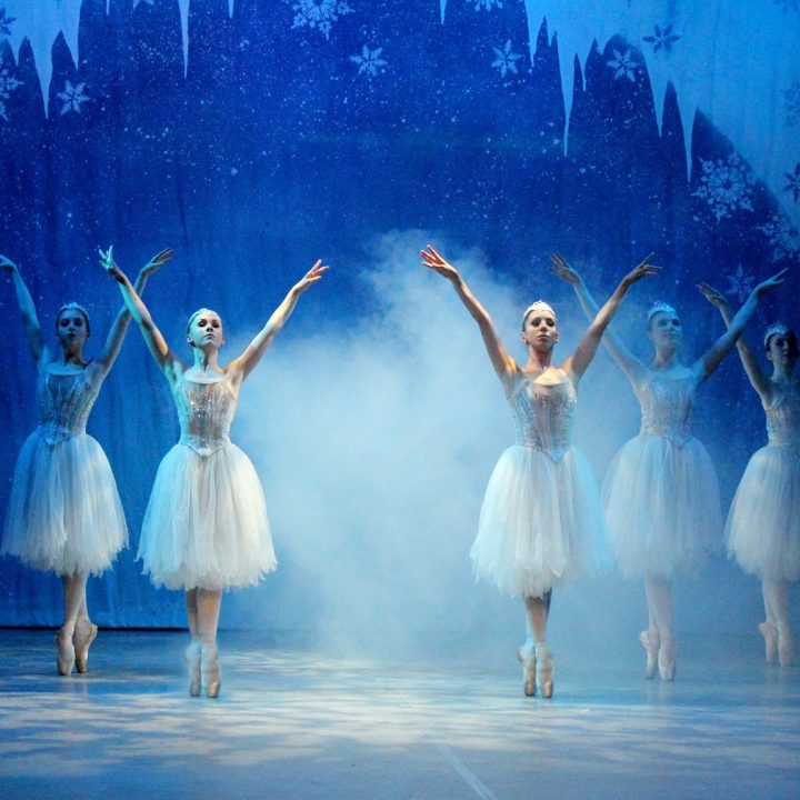 Five ballerinas in white tutus perform on stage.