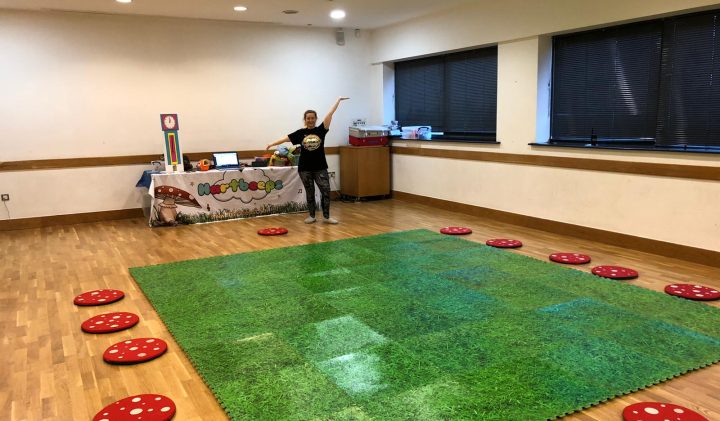 Person lounging on grassy rug with riders, red polka dot cushions, and colourful table display.