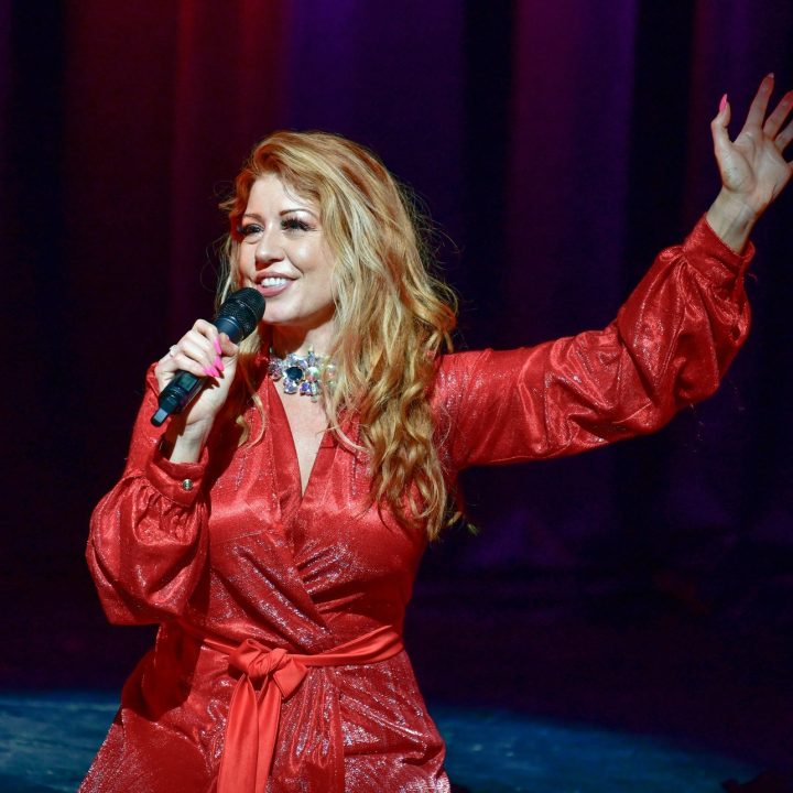 A woman with long, wavy blonde hair, wearing a shiny red dress.