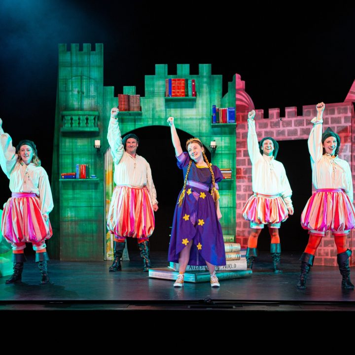 A group of five costumed performers in front of a castle.