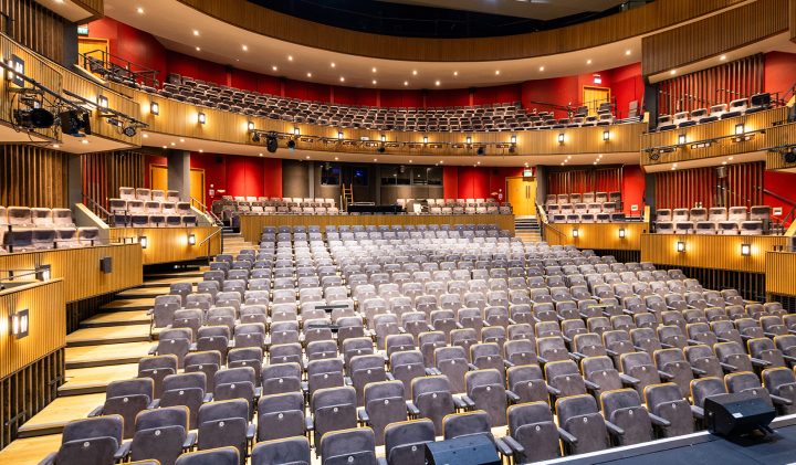 Empty theatre with red walls, wooden accents, and tiered grey seating for film screenings.