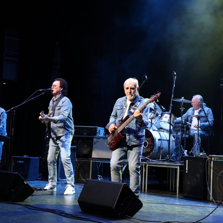 A rock band performs on stage, with four older male musicians.