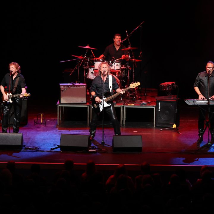 A rock band performs on stage with bright lighting.