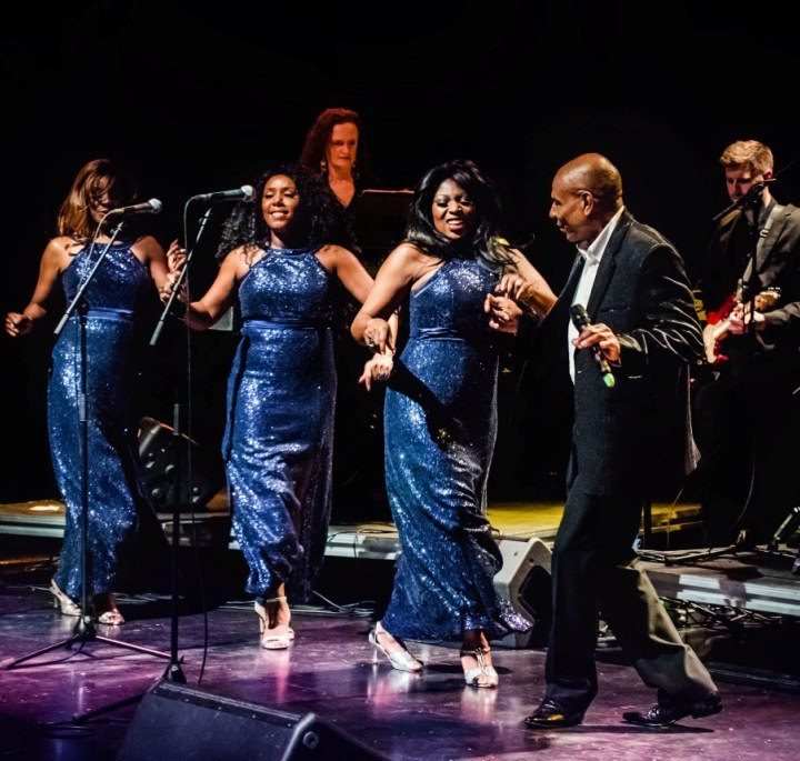 A band is performing on Alban Arena stage. Three women in matching blue sequin dresses.