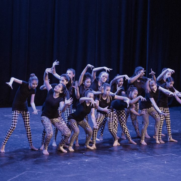A group of young dancers, wearing black tops and patterned leggings.