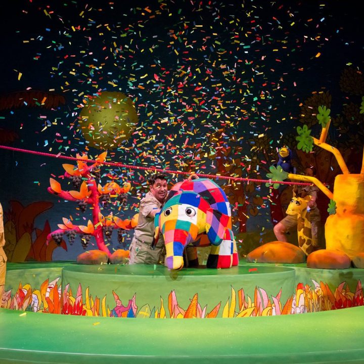 A colourful stage performance featuring actors with puppets.