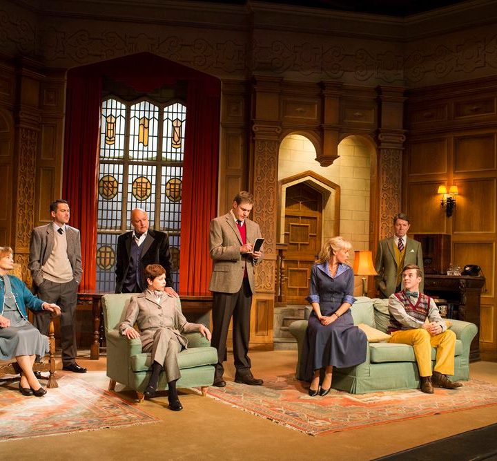 A group of actors dressed in period costumes are on a stage set.