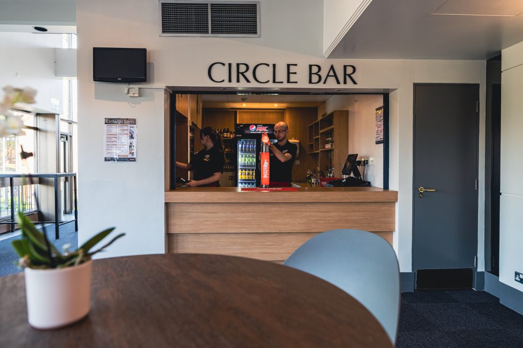 Circle Bar interior with bartenders, drinks fridge, and wooden counter for theatre visit fans.